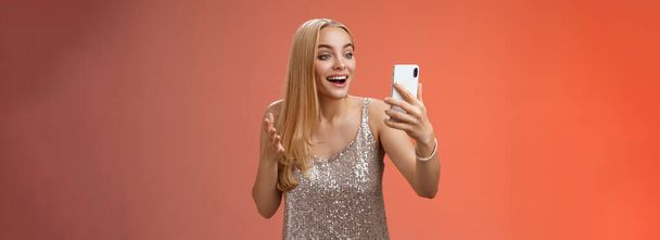 Charming elegant nice blond girl in silver dress talking video call speaking looking smartphone display amused surprised smiling happily have conversation sibling showing prom outfit. - 写真・画像