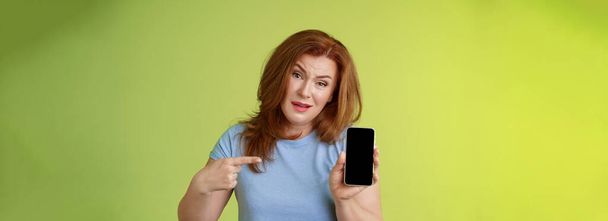 Have something say. Questioned serious-looking displeased redhead mature mother acting pissed hold smartphone pointing blank mobile phone screen demand answers found daughter social-media photos. - Foto, immagini