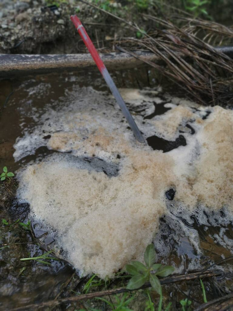 ligne de mousse brunâtre blanche surplombant la rivière de drainage agricole. - Photo, image