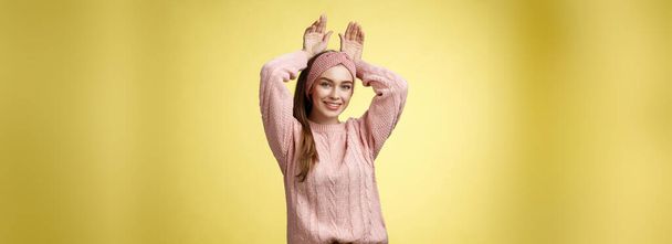 Bella affascinante giocoso giovane femmina europea divertirsi, giocando imitando coniglietto mostrando orecchie di coniglio con le mani dietro la testa, sorridente carino, tenero, felice saluto fidanzato bentornato ove parete gialla. - Foto, immagini