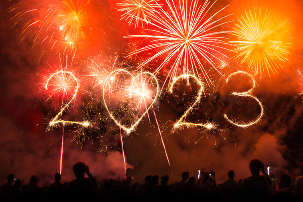 2023 texto de año nuevo hecho con fuegos artificiales y luces de bengala en el cielo nocturno a medianoche. Multitud de personas celebran, concierto escenario y manos arriba en el aire - Foto, imagen