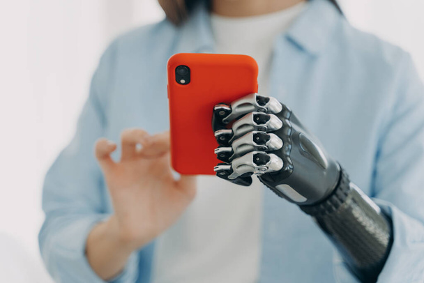Tyttö, jolla on bioninen proteesikäsi, pitää älypuhelinta käsissä. Lähemmäs nainen vammaisuuden säätämällä ele ja ote korkean teknologian robotti keinotekoinen raaja. Mobiilisovellus vammaisille. - Valokuva, kuva