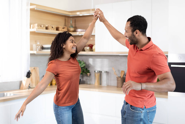 赤いTシャツのダンスで陽気な千年黒のカップルは、キッチンのインテリア、無料のスペースで音楽で一緒に楽しみを持っています。関係、ロマンス、愛と日付、家族は週末と家での余暇を楽しむ - 写真・画像