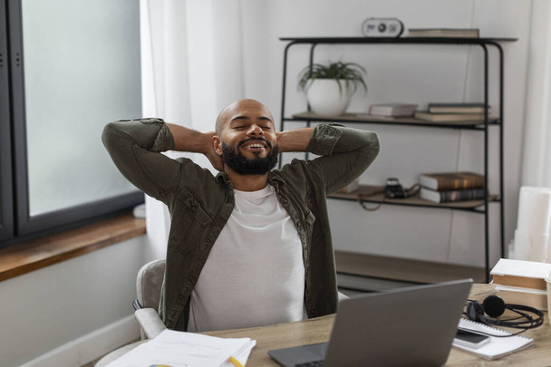 Portrait of happy latin male entrepreneur relaxing at workplace in home office interior, leaning back in chair with hands behind head, resting at desk after working with laptop - Photo, Image