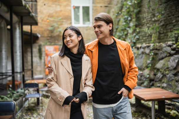 Positive man hugging stylish asian girlfriend in outdoor cafe  - Photo, Image