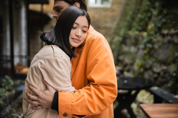 Asian woman hugging stylish boyfriend on terrace of cafe  - Photo, Image