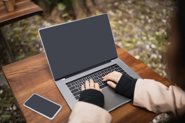 Freelancer desfocado usando laptop com tela em branco perto de smartphone no terraço do café  - Foto, Imagem