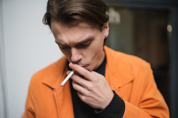 Joven con chaqueta fumando cigarrillo al aire libre  - Foto, Imagen