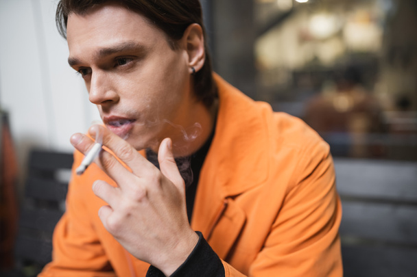 Hombre con chaqueta naranja fumando cigarrillo borroso al aire libre  - Foto, imagen