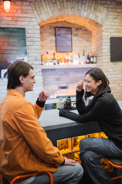Fröhliches gemischtrassiges Paar lacht und redet in der Nähe einer Bar im Café  - Foto, Bild