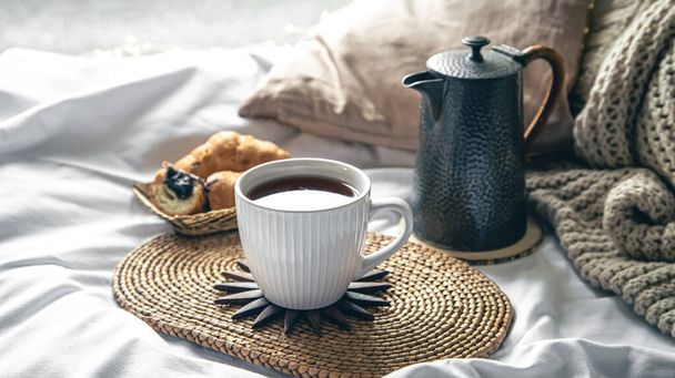 Gezellige huiscompositie met een kopje thee, een theepot en croissants in bed, kopieerruimte. - Foto, afbeelding