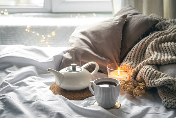 Gemütliche Eigenkomposition mit einer Tasse Tee, einer Teekanne und einer Kerze im Bett. - Foto, Bild