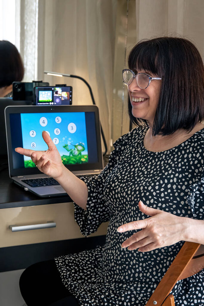 魅力的な中年のブルネットの女性がノートパソコンの画面の前にガラスで、家庭でオンライン、隔離、教育を教えるという概念、子供の心理学者. - 写真・画像