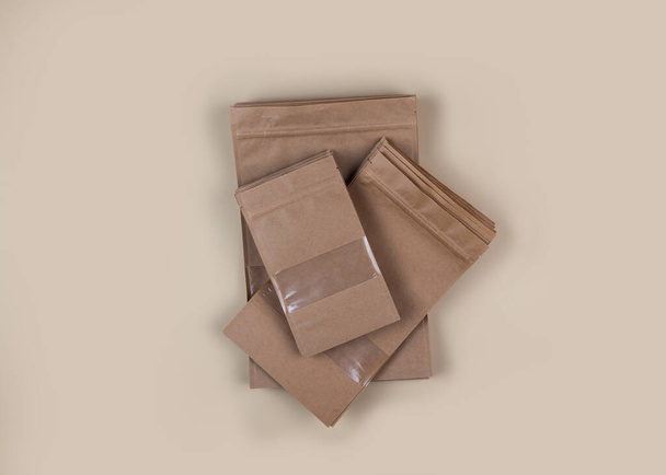 Sacos de papel kraft marrom doypack com vista frontal de mantimentos em um fundo amarelo. Embalagem para alimentos e mercadorias modelo mock-up. Embalagens com janelas para produtos de peso. Vista superior - Foto, Imagem