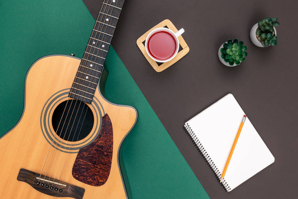 Flache Lage, Akustikgitarre, Tasse Tee und Notizblock auf farbigem Hintergrund, Musikmachen und Kreativitätskonzept. - Foto, Bild