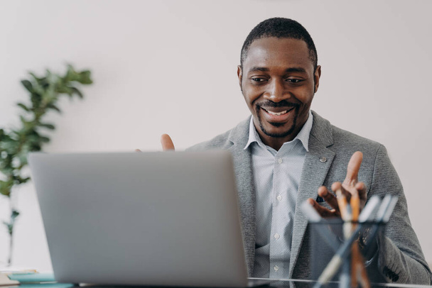 Посмішка приємного афроамериканського бізнесмена, який розмовляє по ноутбуку відео, обговорює роботу, насолоджується розмовою. Бізнес-тренер по бізнесу дружньо працює консультантом в Інтернеті.. - Фото, зображення