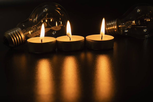 Ηλεκτρική λάμπα και κερί σε σκούρο φόντο. Λαμπτήρας και κερί. Όχι ή διακοπή ρεύματος. Υψηλές τιμές ηλεκτρικής ενέργειας. Εξοικονόμηση. - Φωτογραφία, εικόνα