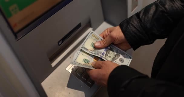 Мужчина считает доллары, снятые с банкомата. Круглосуточное обслуживание. Снятие наличных и банковские операции - Кадры, видео