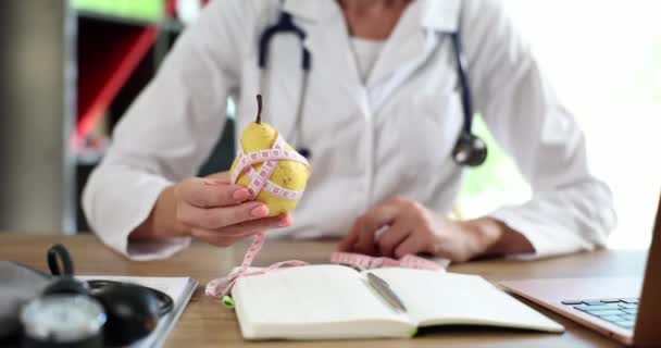 Γιατρός γυναίκα χέρι κρατώντας ταινία μέτρησης γύρω από φρέσκο αχλάδι. Υγιεινός τρόπος ζωής τροφίμων και αθλητισμού - Πλάνα, βίντεο