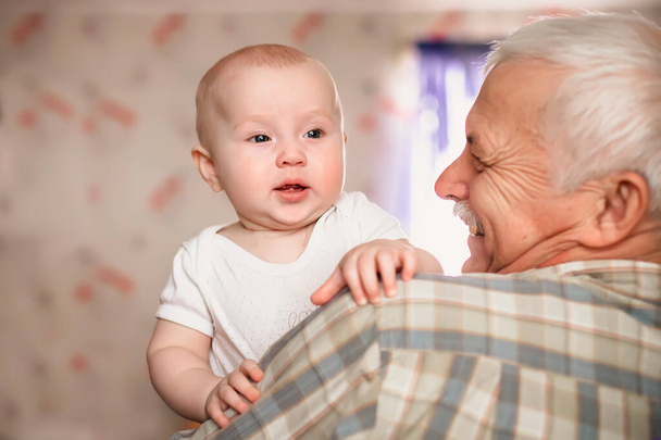 Ein drei Monate altes Baby lächelt komisch. Über die Schulter des Großvaters, der seinen kleinen Enkel hält.. - Foto, Bild