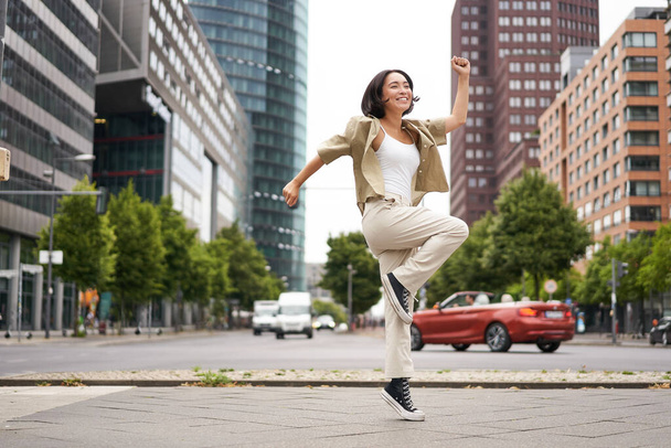 Portret van Aziatisch gelukkig meisje springen en dansen in het centrum van de stad, poseren op straat, uiten vreugde en opwinding. Kopieerruimte - Foto, afbeelding