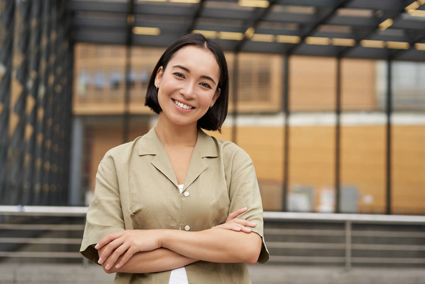 Портрет молодої азійської жінки, що стоїть з упевненістю, перехресть рук на грудях і посміхається, висить на вулиці. - Фото, зображення