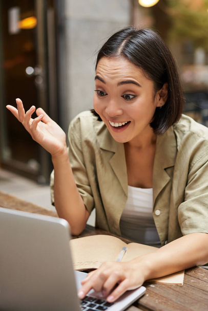 Vertikale Aufnahme eines jungen brünetten Mädchens, das im Videochat chattet, sich online trifft, mit dem Laptop spricht, im Café sitzt. - Foto, Bild