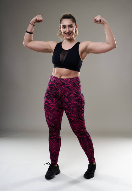 Young plus size hispanic woman posing in fitness attire on gray background - acceptance and inclusiveness - 写真・画像