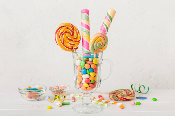 Bunte Bonbons in Tasse auf Tisch auf hellem Hintergrund. Große aufgewirbelte Lutscher. Kreatives Konzept eines Glases voller leckerer Süßigkeiten aus dem Süßwarenladen. - Foto, Bild