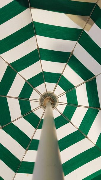 Открытое кафе с зелеными и белыми полосами. Открытый зонтик, защищающий от солнца, зонтик - Фото, изображение