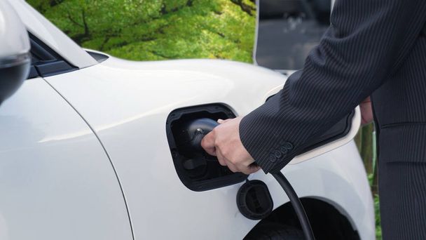 緑の森の充電ステーションから再生可能エネルギーを動力とする電気自動車を充電する事業者の環境意識を高めるための進歩的なキャンペーン。将来の自動車用EV車. - 写真・画像