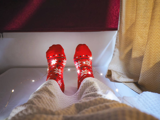 Τουριστική φορώντας κόκκινες κάλτσες με μοτίβο των Χριστουγέννων selfie πόδια στο κρεβάτι στο ξενοδοχείο κάψουλα. Καλές διακοπές σε Χ 'μας έννοια των διακοπών. - Φωτογραφία, εικόνα