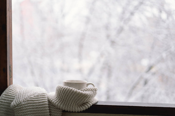 Cozy winter still life. Cup of hot tea with a warm sweater on a vintage wooden windowsill. Cozy home concept. Sweet home. - Photo, Image