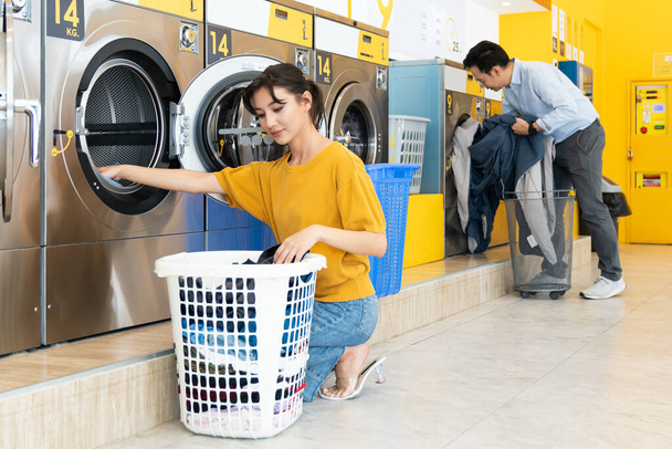 公共の部屋で洗濯機を使って洗濯をしているアジア人。公共の部屋でセルフサービスの商業用洗濯乾燥機の概念. - 写真・画像