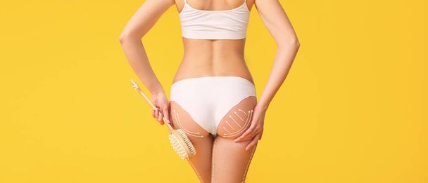 Woman with brush for anti-cellulite massage on yellow background - Photo, Image