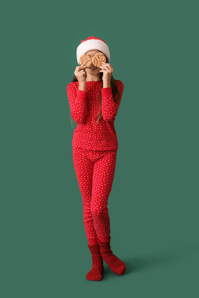 Κοριτσάκι με πιτζάμες και χριστουγεννιάτικα μπισκότα σε πράσινο φόντο - Φωτογραφία, εικόνα