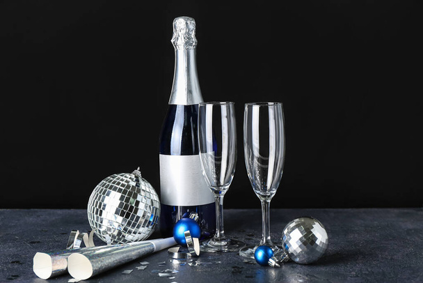 Bardaklar, şampanya şişesi, parti kornaları ve karanlık arka planda Noel topları. - Fotoğraf, Görsel