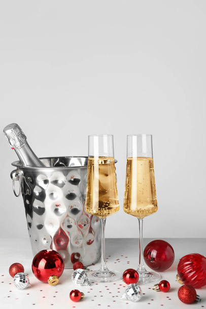 Copos de champanhe, balde com garrafa e bolas de Natal no fundo claro - Foto, Imagem