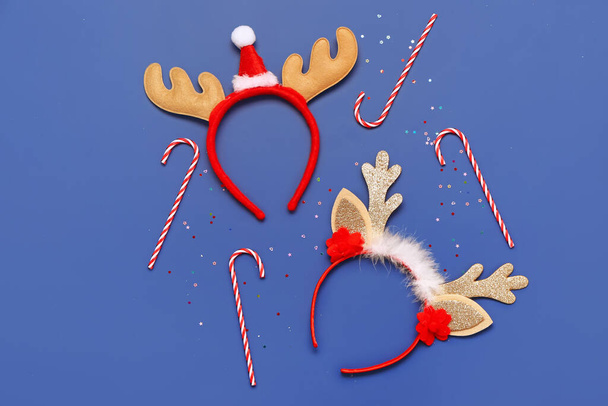 Samenstelling met kerst rendieren hoorns hoofdbanden en snoep stokken op blauwe achtergrond - Foto, afbeelding