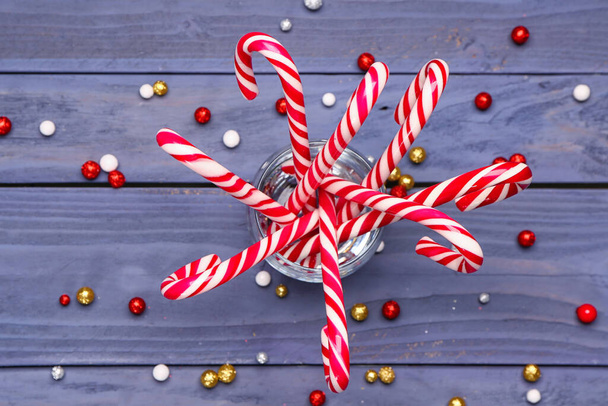 色の木製の背景においしいキャンディーの杖とクリスマスボールを持つガラス - 写真・画像
