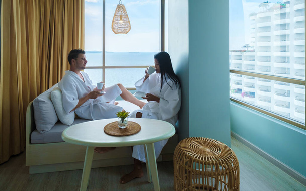 Birkaç Asyalı kadın ve beyaz erkek Tayland 'da okyanusu seyreden bir otel odasında kahve içiyorlar. - Fotoğraf, Görsel