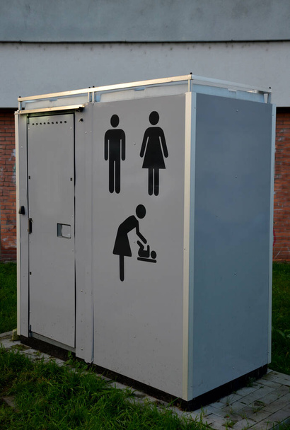 広場のグレーの箱は赤ちゃんと母親のための変化するコーナーとして機能しています。コイン投げの為の有料入り口のある化学タンク付きトイレ。灰色の壁に描かれた絵文字は - 写真・画像