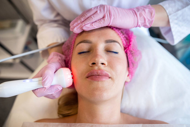 Uma mulher cosmetologista profissional faz uma limpeza ultrassônica do rosto de um paciente em um salão de beleza. Cuidado com a pele. Limpeza facial - Foto, Imagem