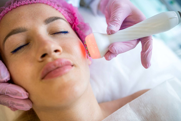 Tyttö kosmetologin vastaanotolla pesee kasvojaan ultraäänellä. Ultraäänipuhdistus on laitteiston puhdistus, joka suoritetaan korkean taajuuden ultraääniaaltojen avulla. - Valokuva, kuva