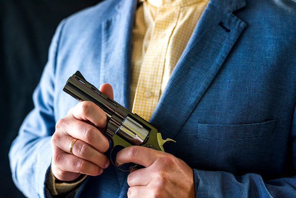 Περικοπή πορτρέτο του ανδρικού σωματοφύλακα σε σμόκιν κρατώντας όπλο για την άμυνα. σωματοφύλακας με κομψό σμόκιν. Ρεβόλβερ στα χέρια. κοντινό πλάνο φωτογραφία απομονωμένη σε μαύρο φόντο - Φωτογραφία, εικόνα