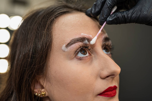 um artista da sobrancelha está laminando as sobrancelhas de um cliente bonito. Sobrancelhas pintura de sobrancelha laminação - Foto, Imagem