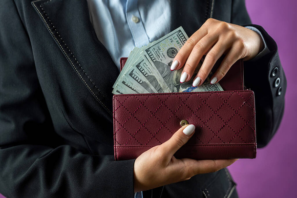 Primo piano delle mani di una donna che mette una banconota da cento dollari nella borsa. Concentrati sulla borsa. soldi. dollari nel portafoglio - Foto, immagini