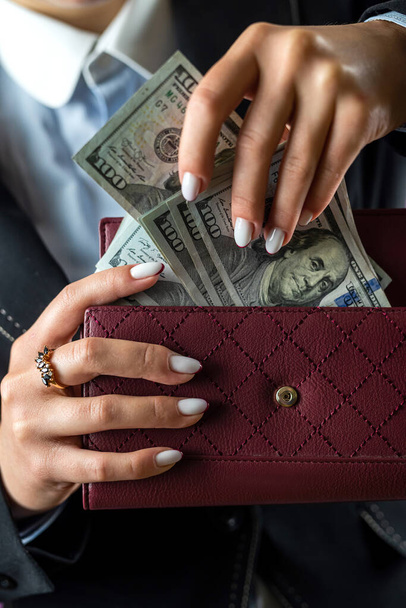 Nahaufnahme einer weiblichen Hand, die eine schwarze Brieftasche hält, in der sich Dollars befinden. Frau mit Dollargeld im Geldbeutel - Foto, Bild
