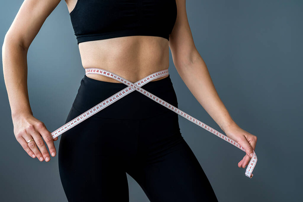 Спортивная стройная женщина измеряет талию рулеткой после диеты, изолированной на сером фоне. Диетическая концепция. женщина сбрасывает лишний вес - Фото, изображение