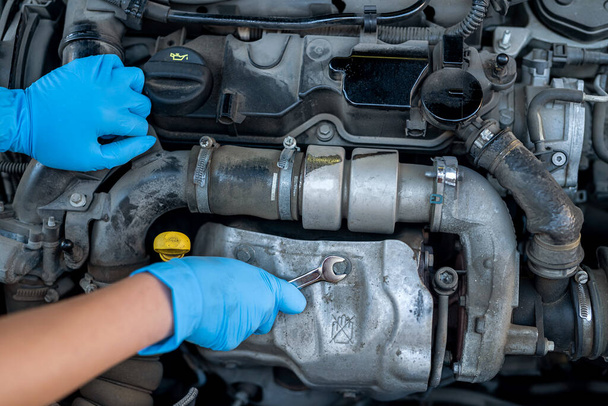 Hände einer Mechanikerin, die unter der Motorhaube eines Autos in einem Autoservice arbeitet. Ermächtigung einer Frau in Handschuhen in der Nähe eines Autos. - Foto, Bild